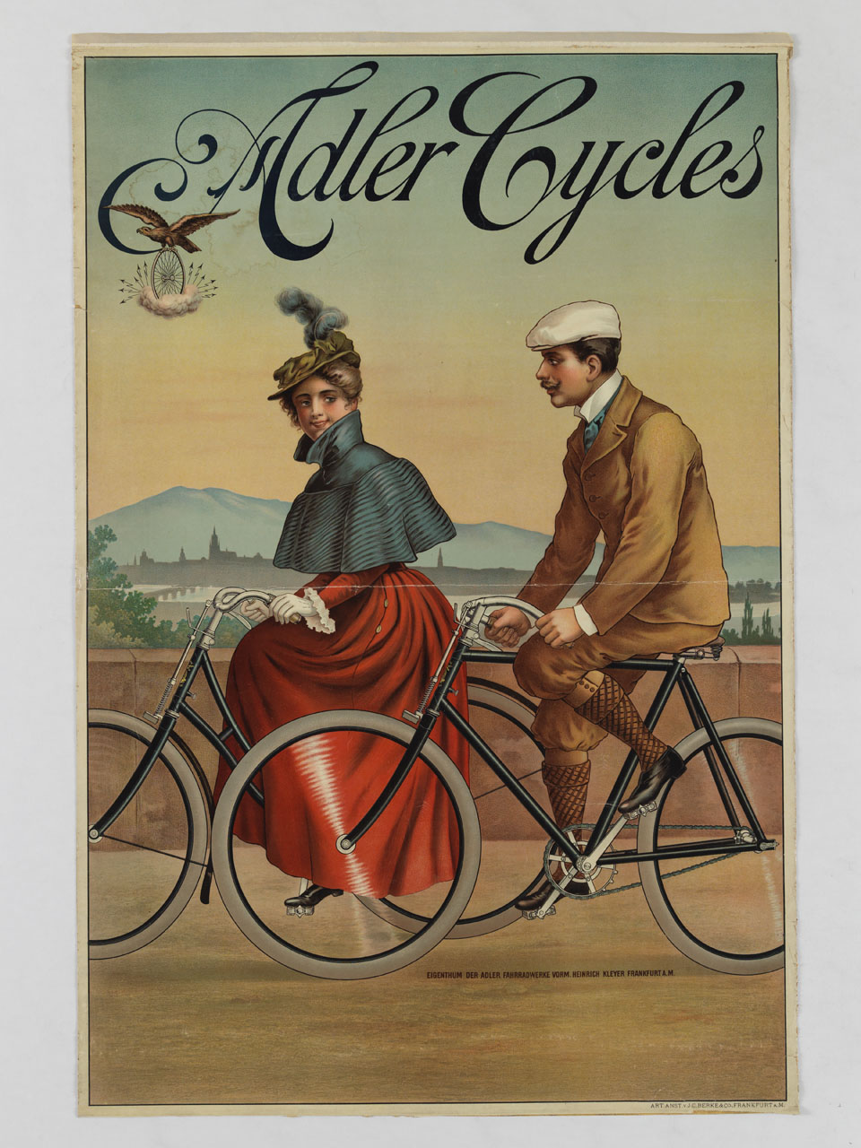 una coppia passeggia in bicicletta sullo sfondo di una città bagnata dal fiume (manifesto) - ambito tedesco (sec. XX)
