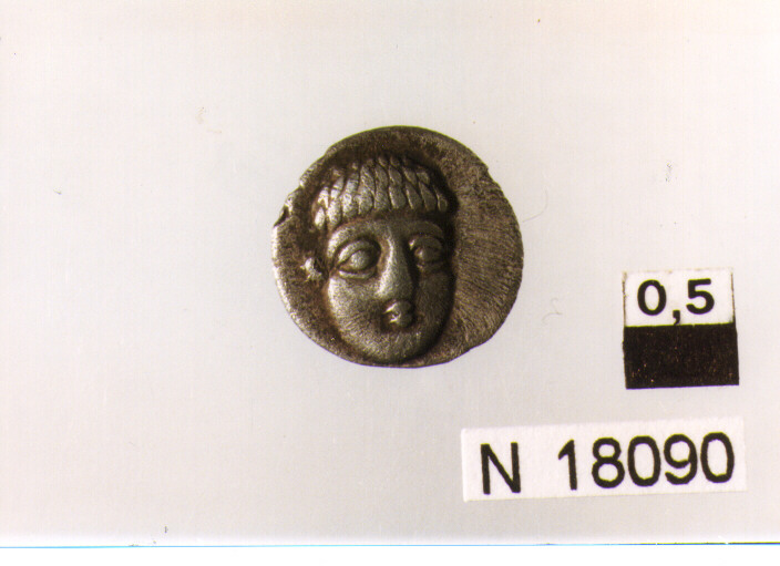 R/ testa virile imberbe di fronte con capelli corti e arricciati; V/ delfino, chicco di grano e arsella (obolo) (sec. IV a.C)