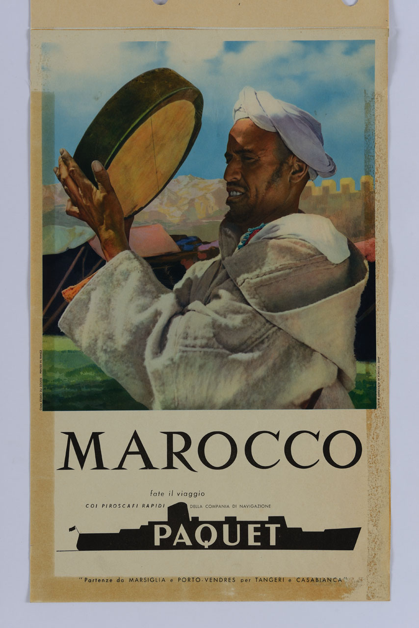 un abitante del Marocco con la tipica tunica djallaba e il turbante suona il bendir; sullo sfondo le tende di una tribù, le montagne e un muro merlato (manifesto) di Studios du Souissi (sec. XX)