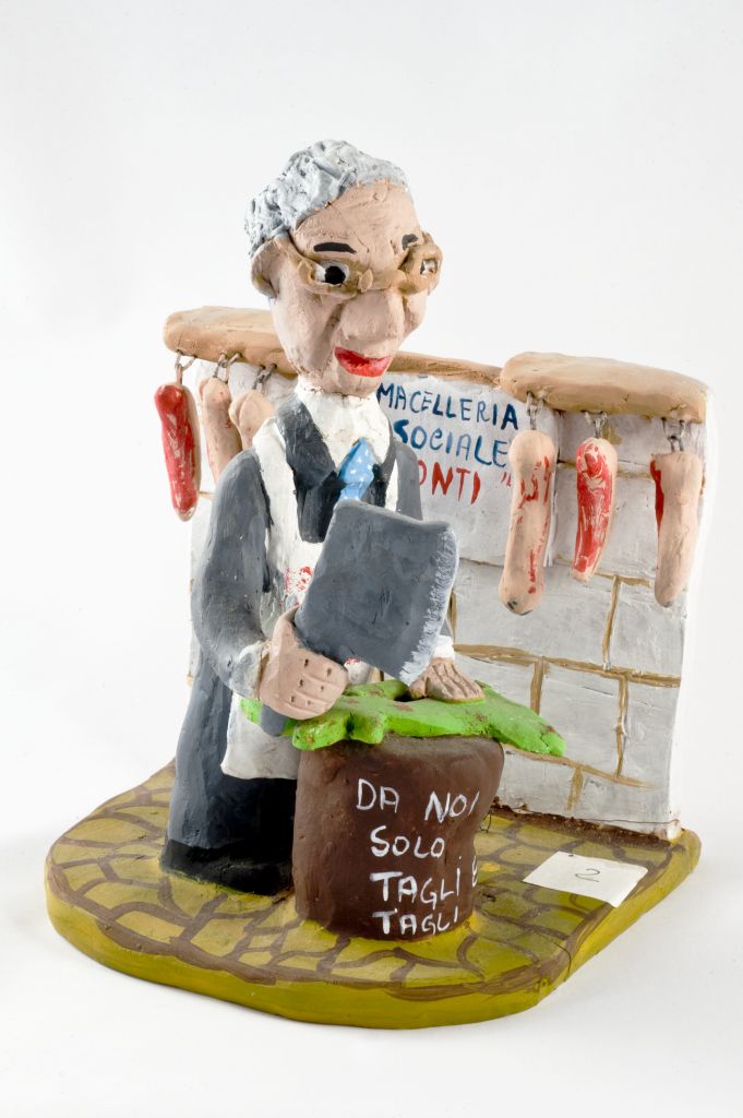 Macelleria sociale Mario Monti, figura con grembiule bianco e mannaia in mano (fischietto, a fessura interna, strumenti musicali) di Pastore P, Grazzi M - scuola, scuola (2012, 2012)