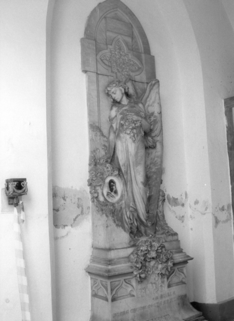 Angelo che porge fiori al ritratto fotografico della defunta (stele funeraria) di Zilocchi Giacomo (sec. XX)