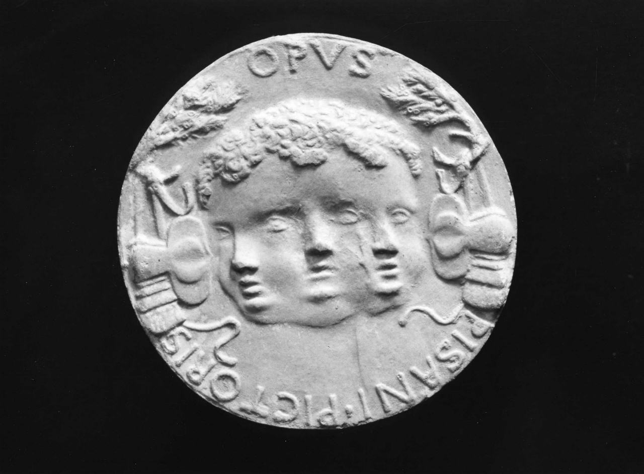 testa con tre volti infantili tra ginocchielli d'armatura sospesi a rami di ulivo (calco di medaglia) di Lelli Oronzio (bottega) (sec. XIX)