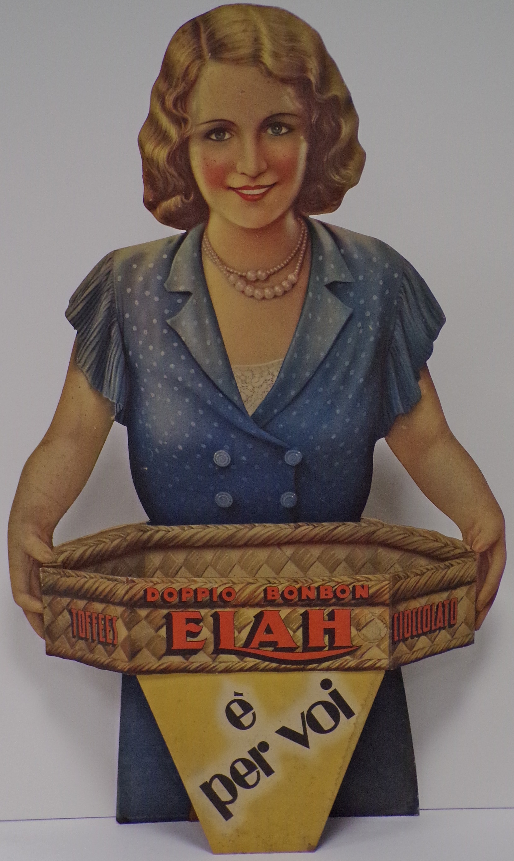 Doppio Bonbon, toffees, cioccolato Elah: è per voi, giovane donna sorridente offre i prodotti Elah entro una cesta di vimini (Cartello - da vetrina, opera isolata) - ambito torinese (prima metà XX)